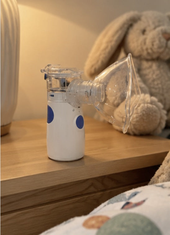 Portable nebuliser with a mask on a bedside table beside a teddy bear